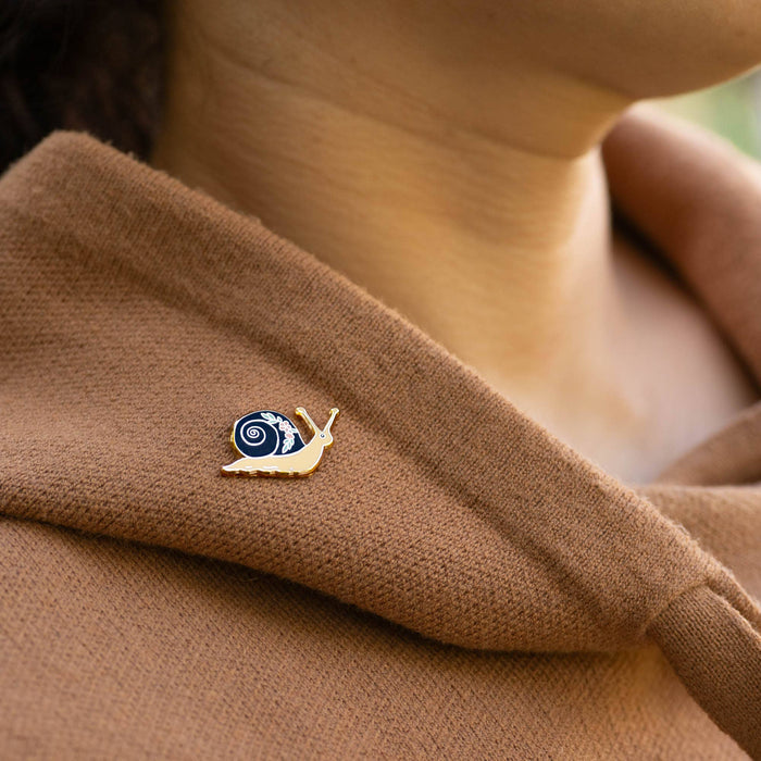 Garden Snail enamel pin with blue spiral shell on brown knit fabric