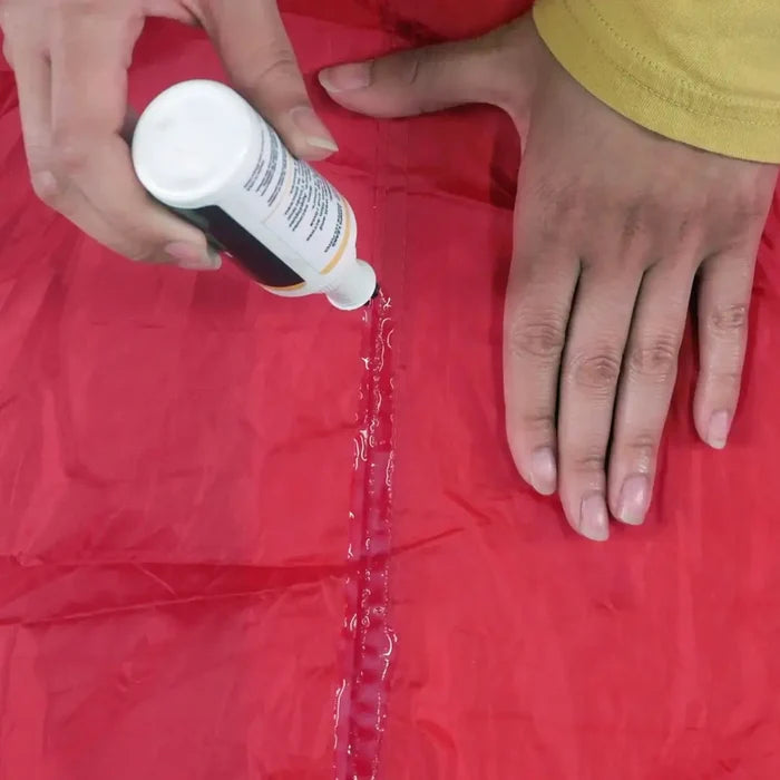 Person applying Gear Aid Seam Grip + FC Fast Cure Seam Sealant to a red fabric.