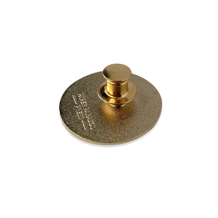 Back of a gold Get Sh*t Done enamel pin showing the textured disk and round pin post.