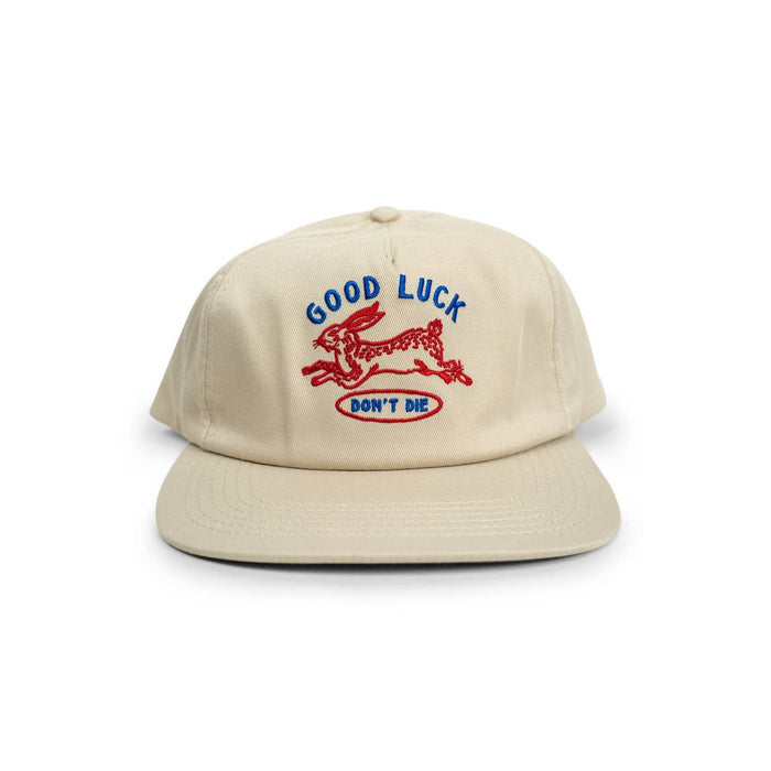 Beige cap with blue Good Luck text and red running dog embroidery and Don't Die in a blue oval on the front