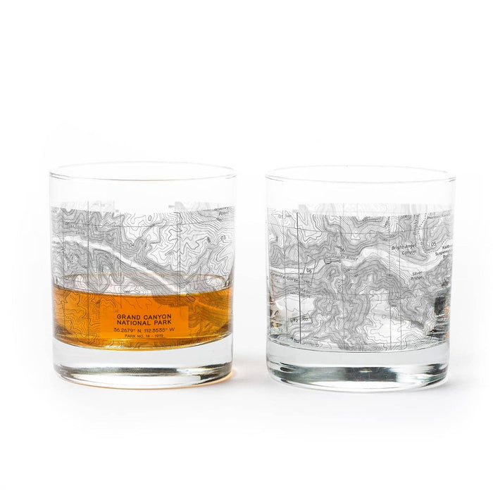 Two clear whiskey glasses featuring Grand Canyon topographic maps, one with amber liquid.