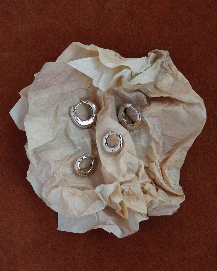 Silver hoop earrings on crumpled beige tissue paper against a brown background