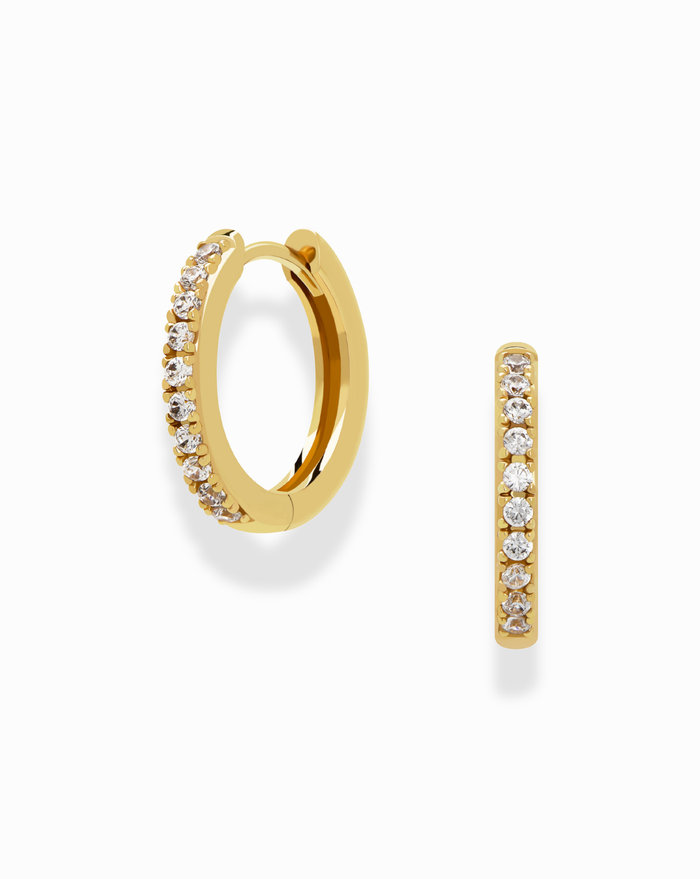 The Grande Reese Hoops by Mod + Jo feature two gold pave hoops, each lined with sparkling white topaz on the front edge. One earring is upright to showcase the stones; the other displays its circular form in tarnish-resistant 14k gold.