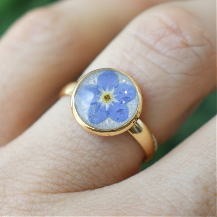 Blue pressed flower cabochon set in a gold adjustable ring worn on a finger