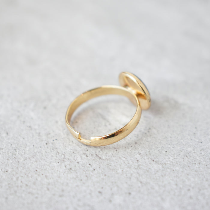 Gold adjustable band ring resting on a light textured surface