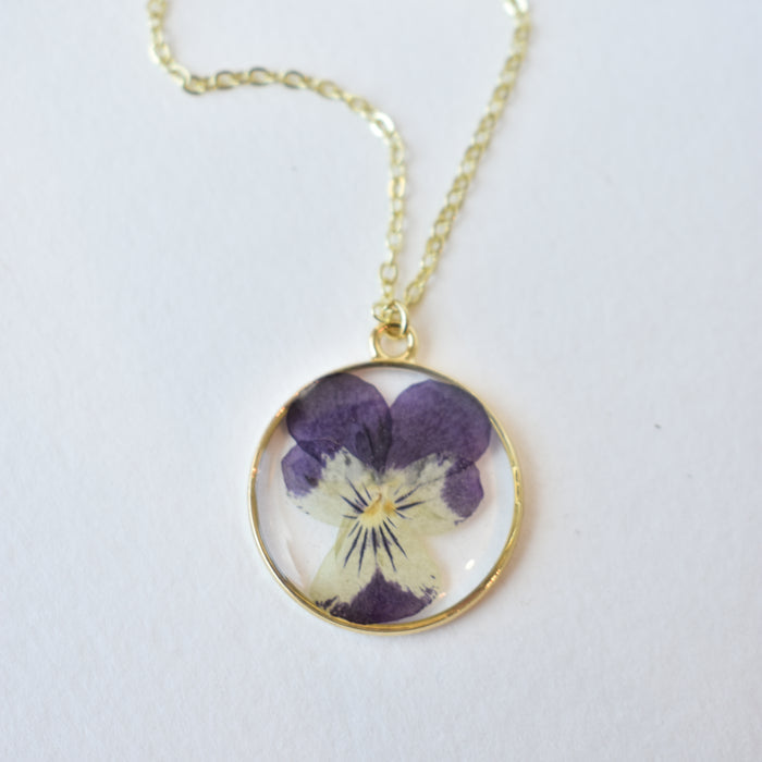 Handmade necklace with an oval gold bezel pendant housing a pressed violet flower on a delicate gold chain.