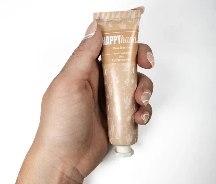 Hand holding a peach tinted tube of Happy Hands Rose Blossom hand lotion with cactus pattern