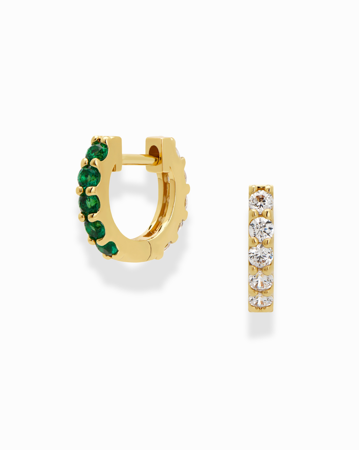 The Harlow Reversible Birthstone Huggies by Mod + Jo are small 18k gold-plated hoop earrings: one features green gemstones, the other clear white stones, both shown on a white background.