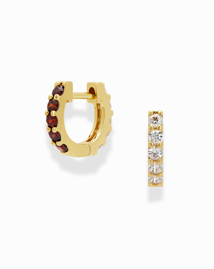 The Harlow Reversible Birthstone Huggies by Mod + Jo are small gold-plated hoops—one set with round red gems, the other with round clear gems in a row—offering a playful twist on classic style.