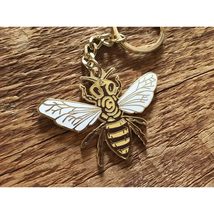 Gold honey bee keychain with white enamel wings on a wood surface