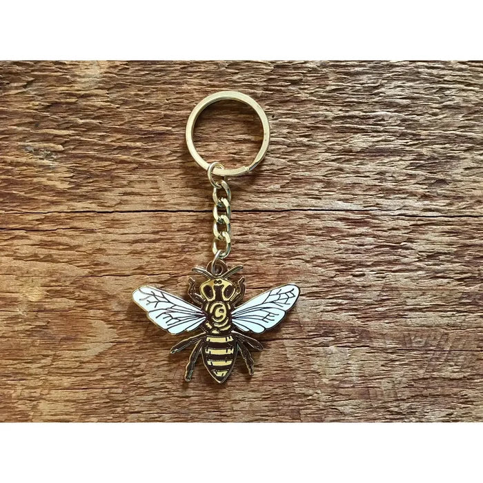Gold honey bee keychain with ring and chain on a wood surface
