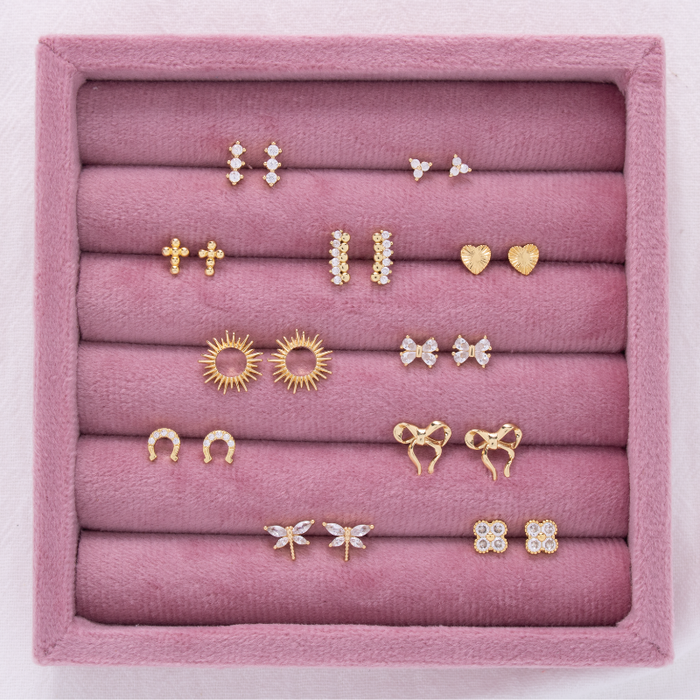 Pink velvet jewelry tray showing multiple pairs of gold and diamond stud earrings in various shapes