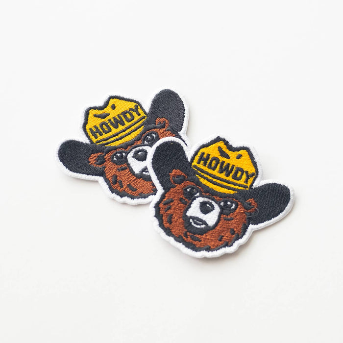 Overlapping Howdy the Bear patches featuring a bear head with a yellow shield and HOWDY lettering