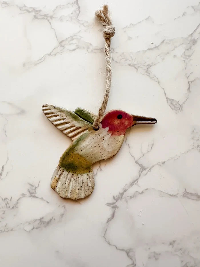 Ceramic hummingbird ornament with red head and green body hung by twine.