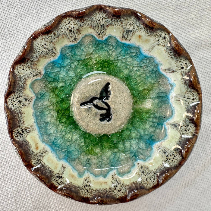 Circular ceramic hummingbird trinket tray with a beige center black silhouette of a hummingbird and green crackle glaze extending to a brown rim