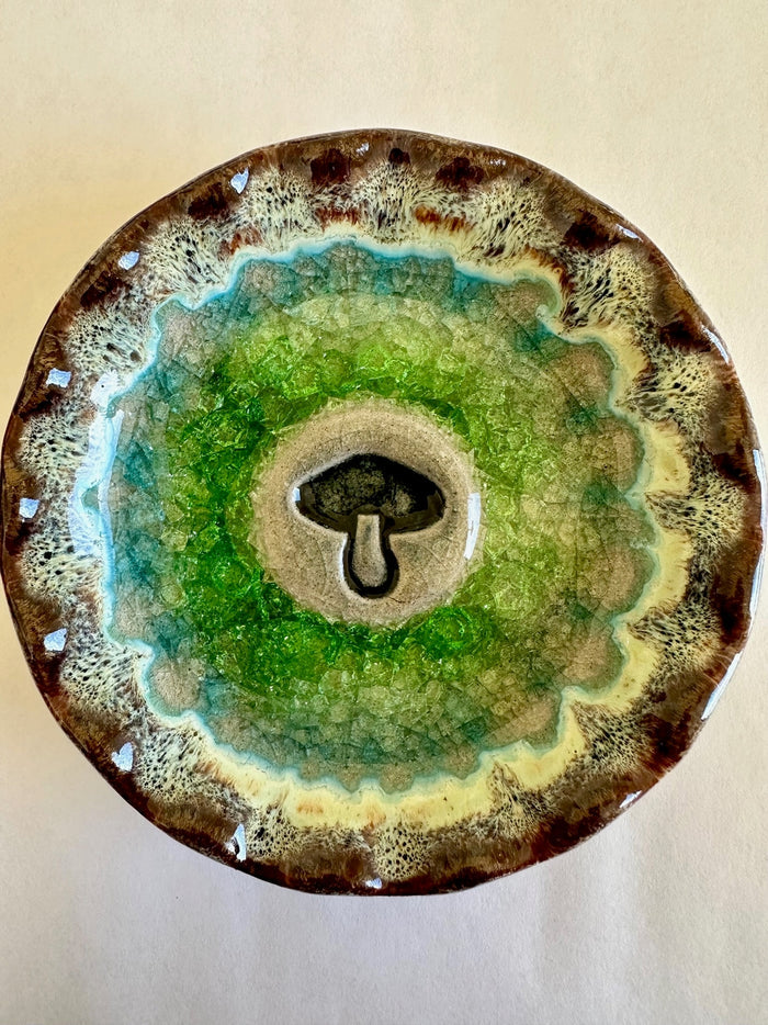 Circular ceramic mushroom trinket tray with a beige center and black mushroom silhouette, surrounded by crackled green and turquoise glaze.