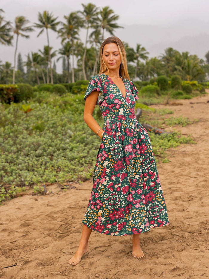 Model wearing Isla Dress with a deep V neckline and flutter sleeves in a tropical garden with palms