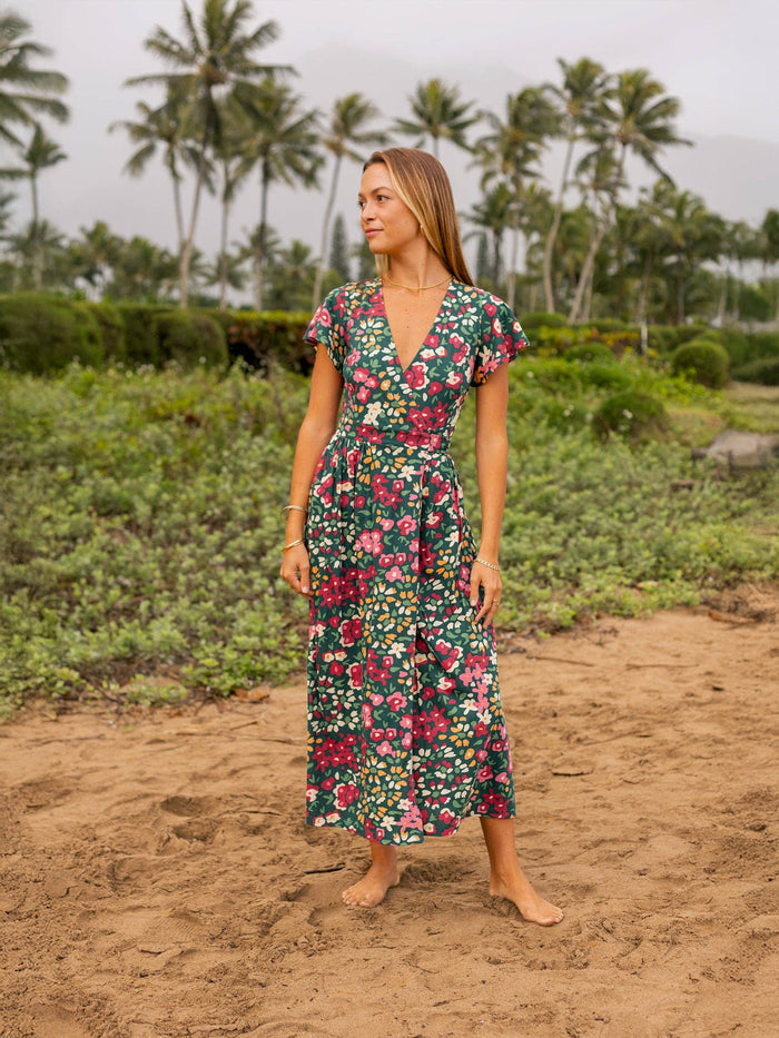 Isla Dress in green floral print that falls to mid calf as the model walks barefoot on the sandy path