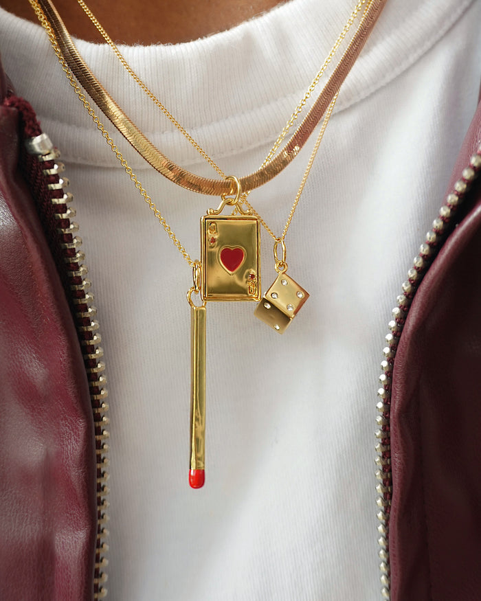 Jenna Dice charm necklace shown with layers of gold jewelry, card and matchstick charms, and a maroon jacket.