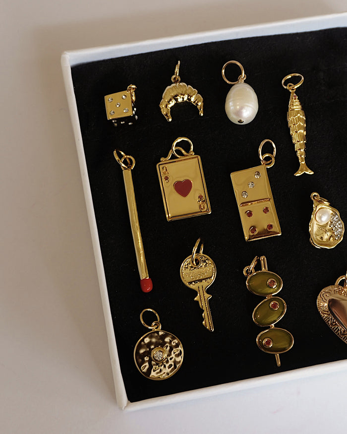 Gold Jenna Dice Charm, along with croissant, key, heart & other luxury-themed jewelry charms showcased in a box.