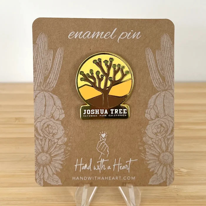 Joshua Tree enamel pin featuring a circular desert scene with a stylized tree and a labeled base.