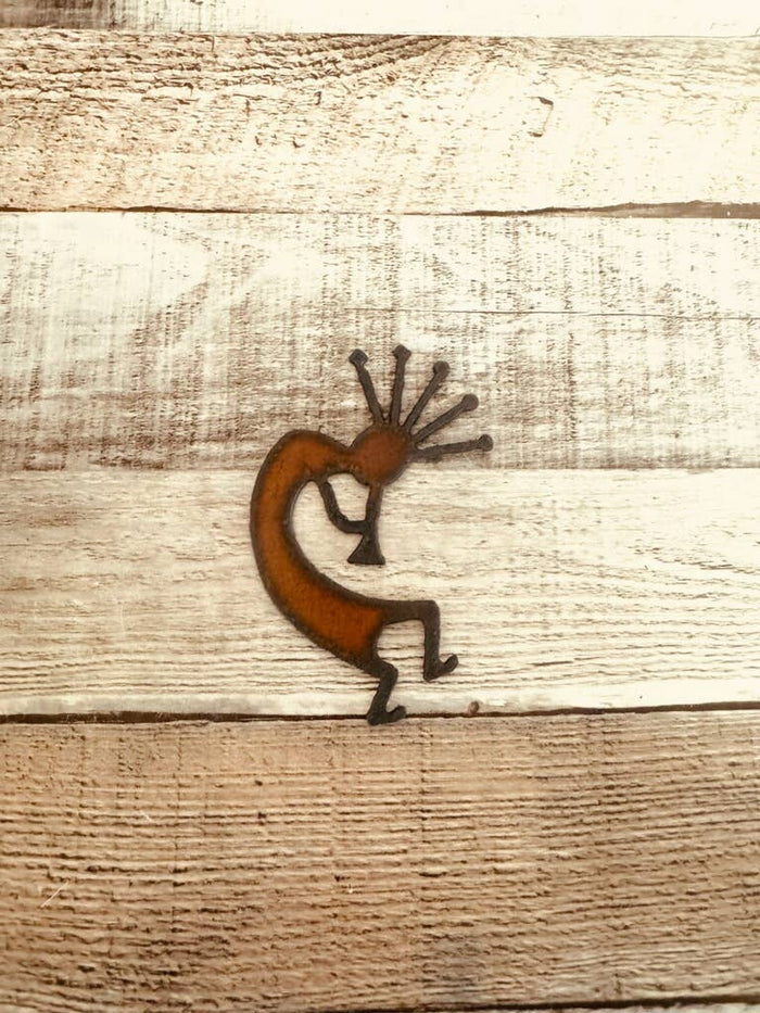 Rusty metal Kokopelli magnet shaped as a dancing figure on a light wood background