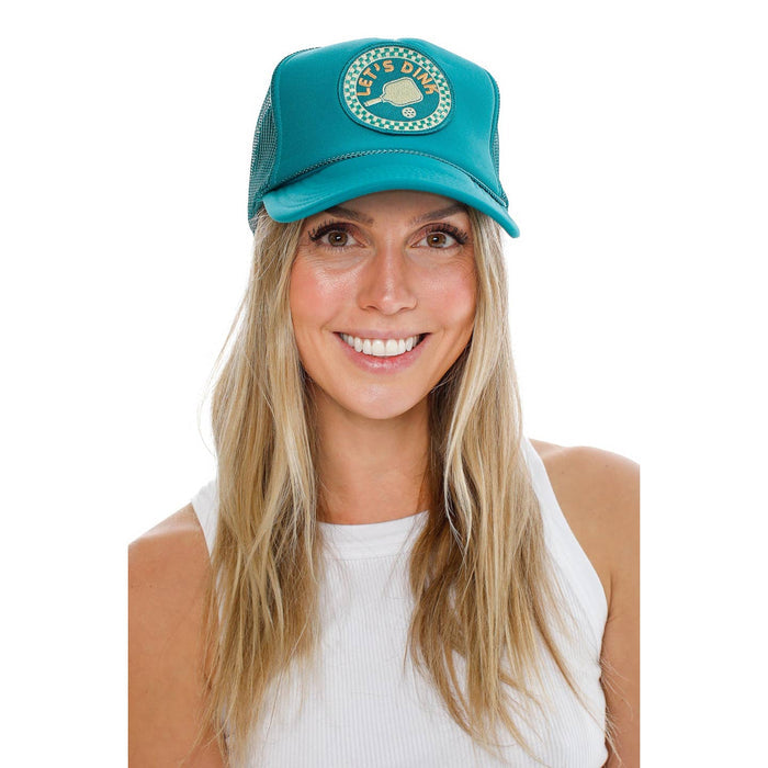 Smiling woman wearing teal trucker hat with a circular patch on the front