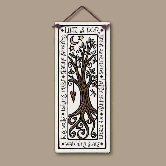 Vertical ceramic wall art showing a tree and winding road on a framed landscape with the Life is For phrase.
