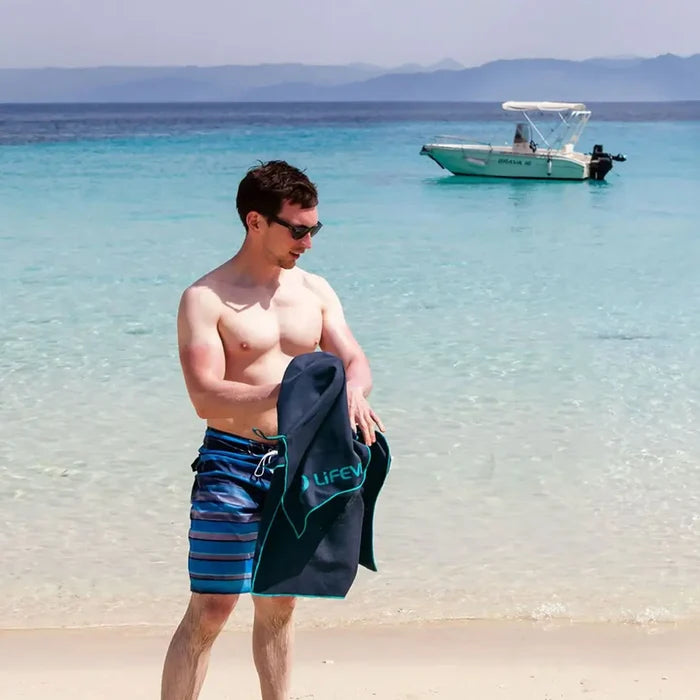 Man in shorts on the beach drying himself with a xlarge Lifeventure SoftFibre recycled travel towel in grey