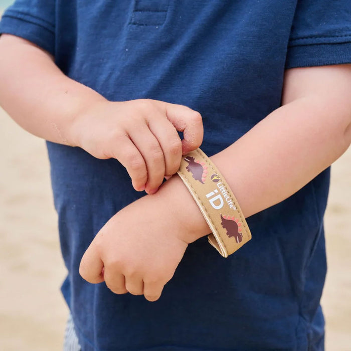 Lifestyle shot of a child putting on their Littlelife Dinosaur identification wristband