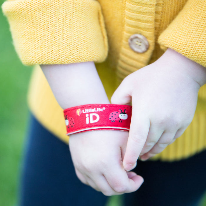 Lifestyle shot of a child putting on their Littlelife Ladybird identification wristband