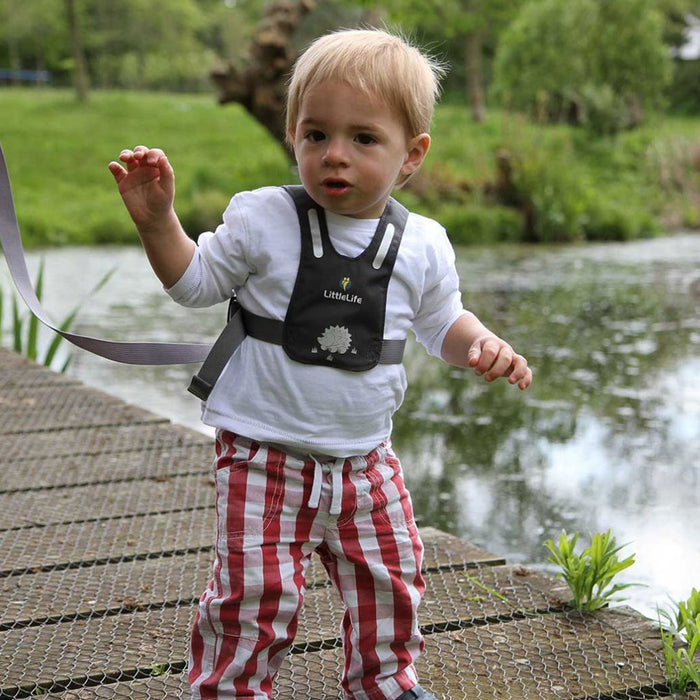 Lifestyle shot of a toddler walking outside using the Littlelife reflective toddler safety reins with the adult safety strap attached