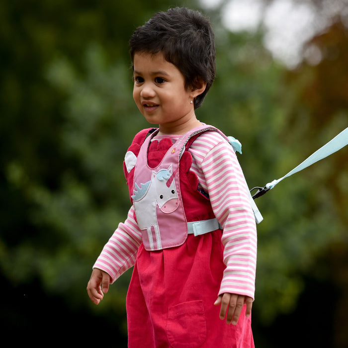 Lifestyle shot outdoors of a toddler wearing a Littlelife unicorn toddler safety reins with the adult strap connected to the reverse