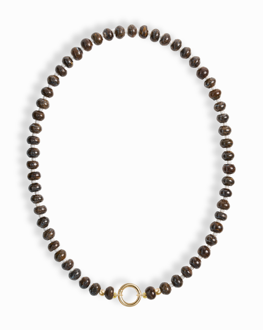 The Macey Gemstone Necklace by Mod + Jo features evenly spaced dark brown round beads and a simple 14k gold-plated circular clasp at the center, displayed on a white background.