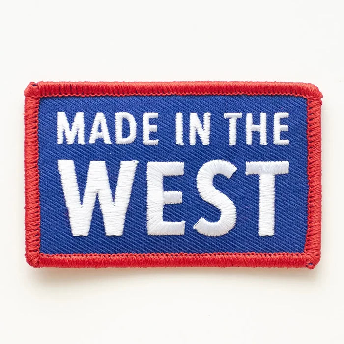 Blue rectangular embroidered patch reading MADE IN THE WEST in bold white letters with a red stitched border.
