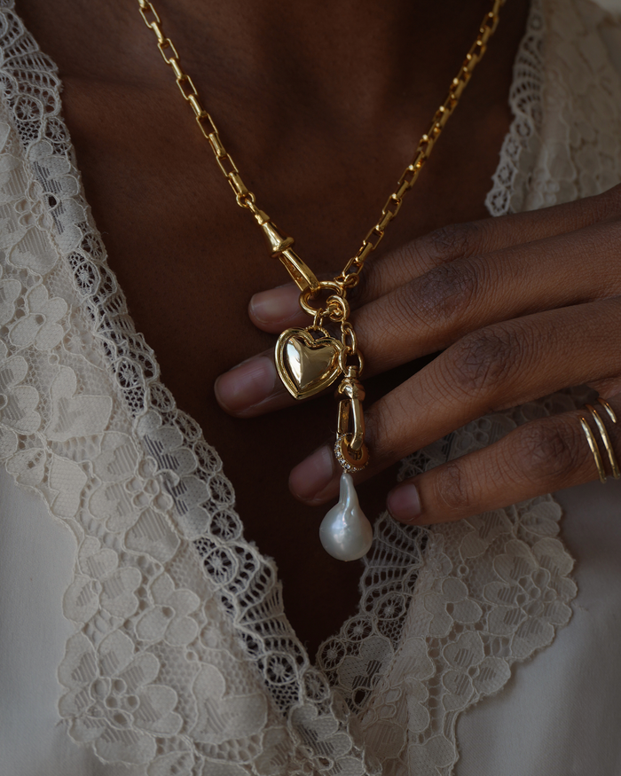 Gold necklace with a heart pendant and pearl drop on a lace fabric background