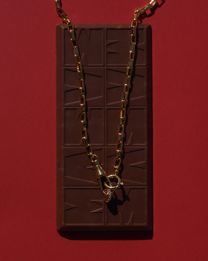 Gold chain necklace on a chocolate bar against a red background