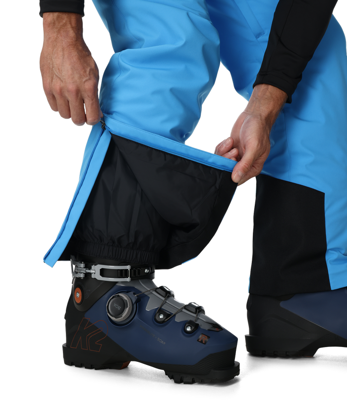 Person wearing blue pants and black ski boot with gaiters on a white background