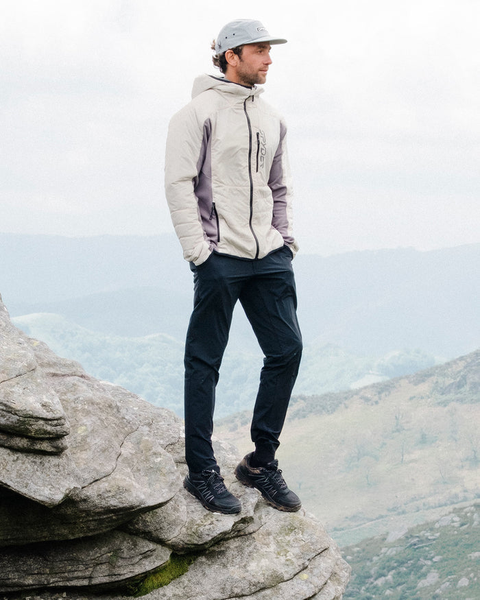 Man in outdoor clothing standing on a rocky outcrop with a mountainous landscape in the background