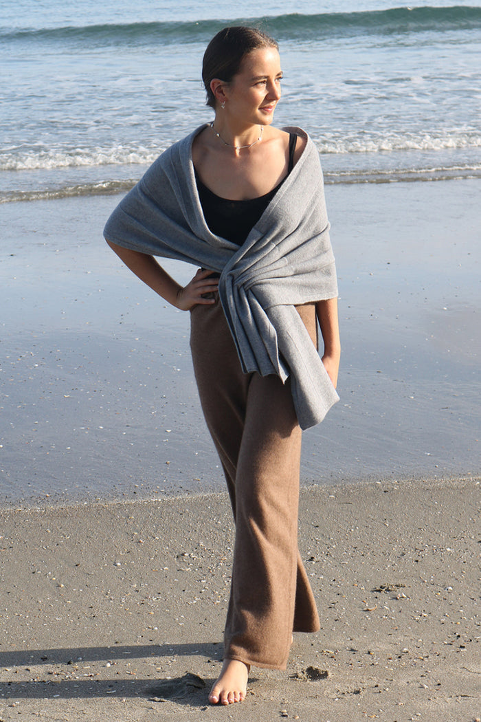 A woman standing on a beach wearing black merino active pants and a light-colored sweater.