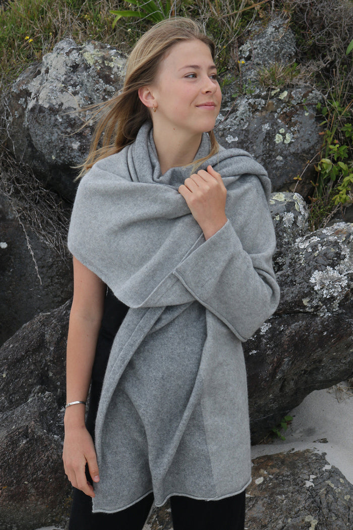 A woman standing outdoors wearing a gray Merinosilk travel wrap that is draped over her shoulders.