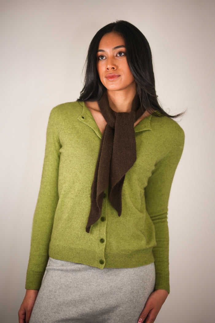 Woman wearing a green cardigan and brown scarf against a plain background