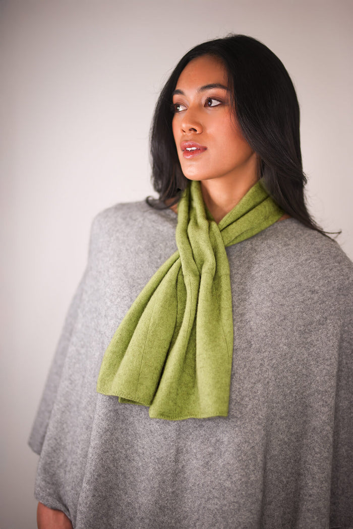 Woman wearing a green scarf and gray poncho against a plain background