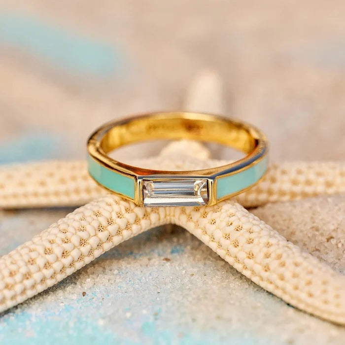 Two-tone gold ring with turquoise enamel sides and a rectangular clear stone resting on a beachy starfish backdrop.