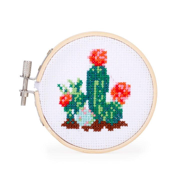 Close up of cactus embroidery in a wooden hoop on white fabric with green cactus and red flowers.