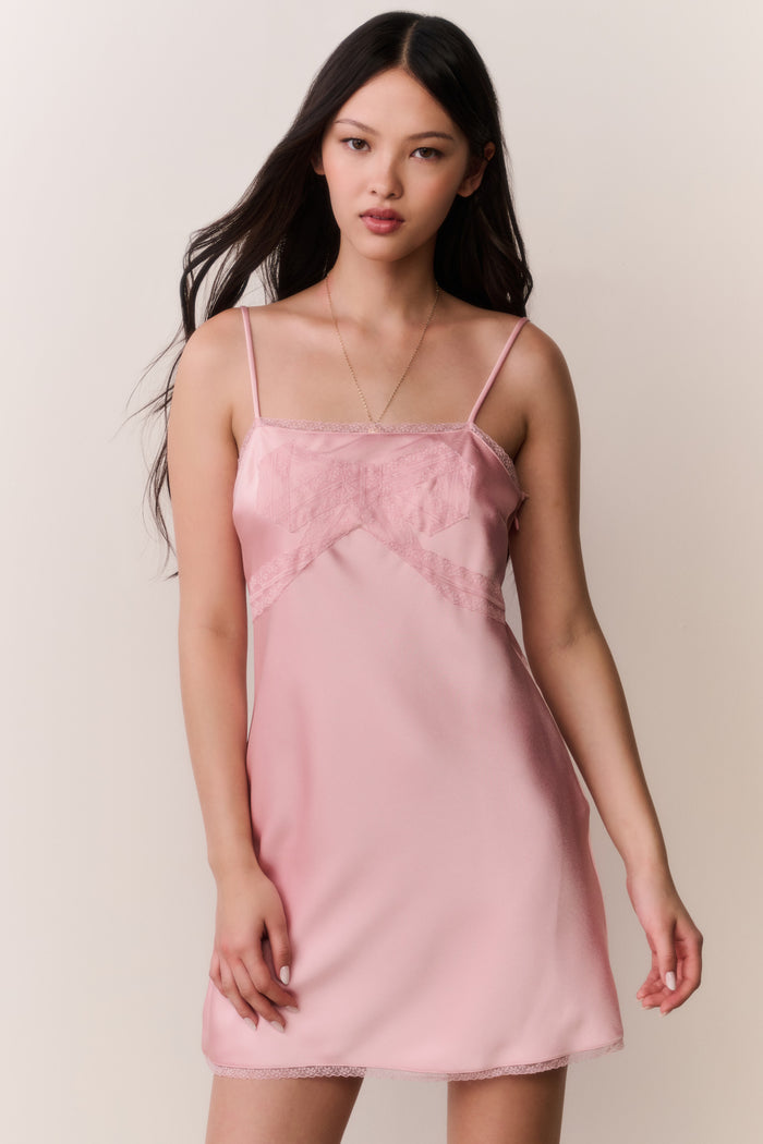 Woman wearing a pink satin slip dress with bow design against a plain background