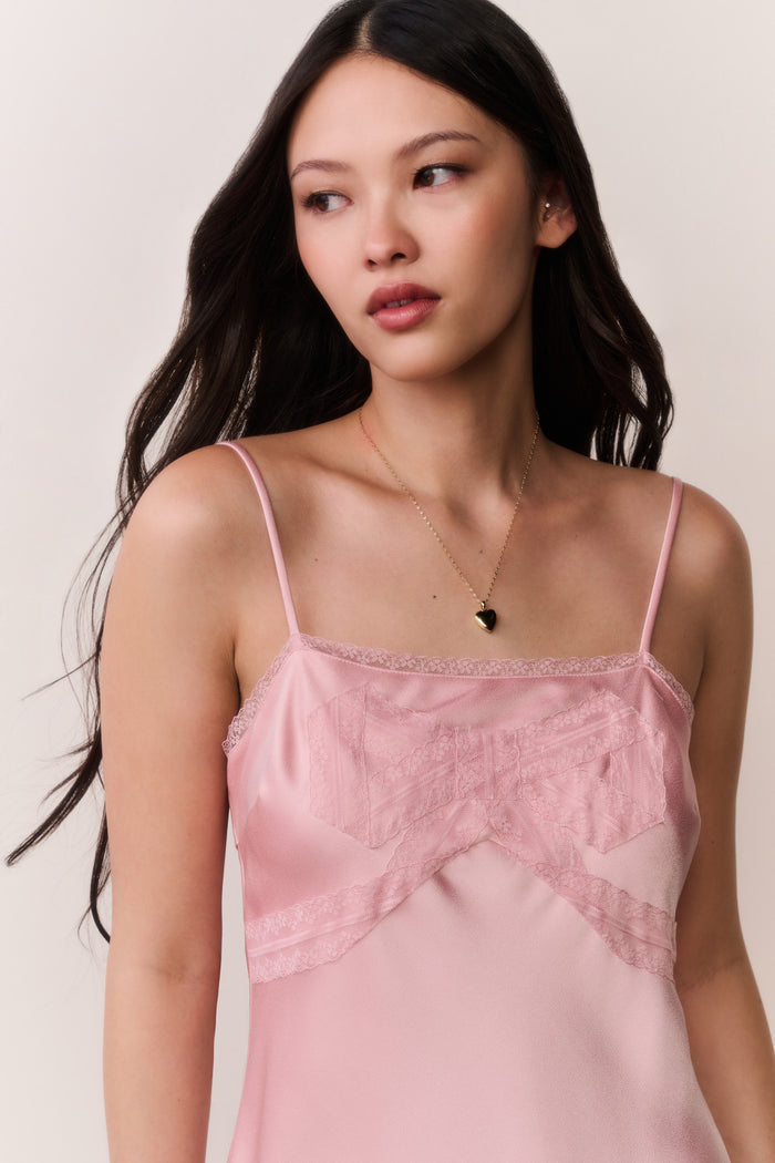 Woman wearing a pink satin slip dress with bow design against a plain background