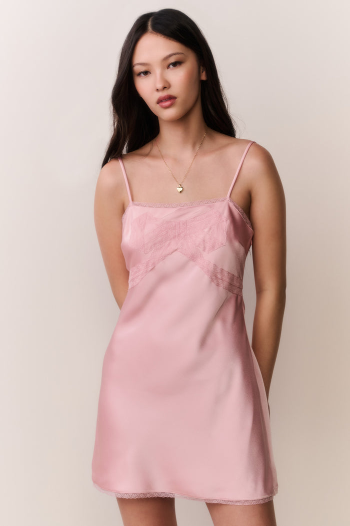 Woman wearing a pink satin slip dress with bow design against a plain background