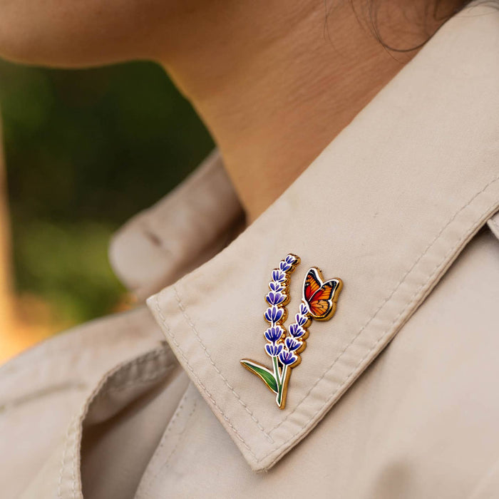 Beige jacket lapel featuring two Monarch And Lavender enamel pins lavender sprig and butterfly