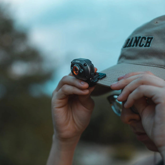Lifestyle shot of a man attaching a NEBO Mycro rechargeable 400 lumens LED head torch to their cap at twilight